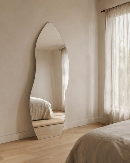 Allira curved full length mirror leaning in a bedroom by sheer curtains