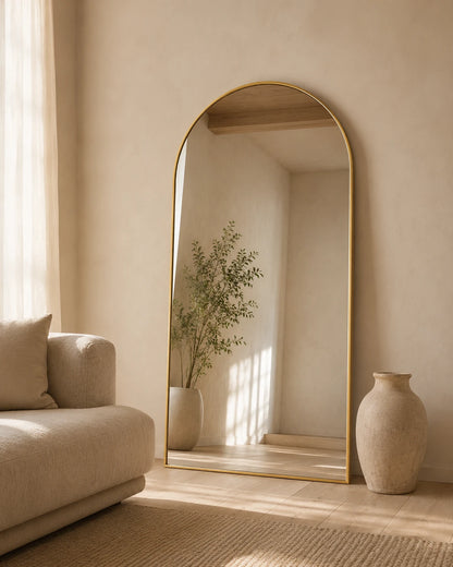 Sienna oversized arch mirror leaning behind a sofa beside tall vases